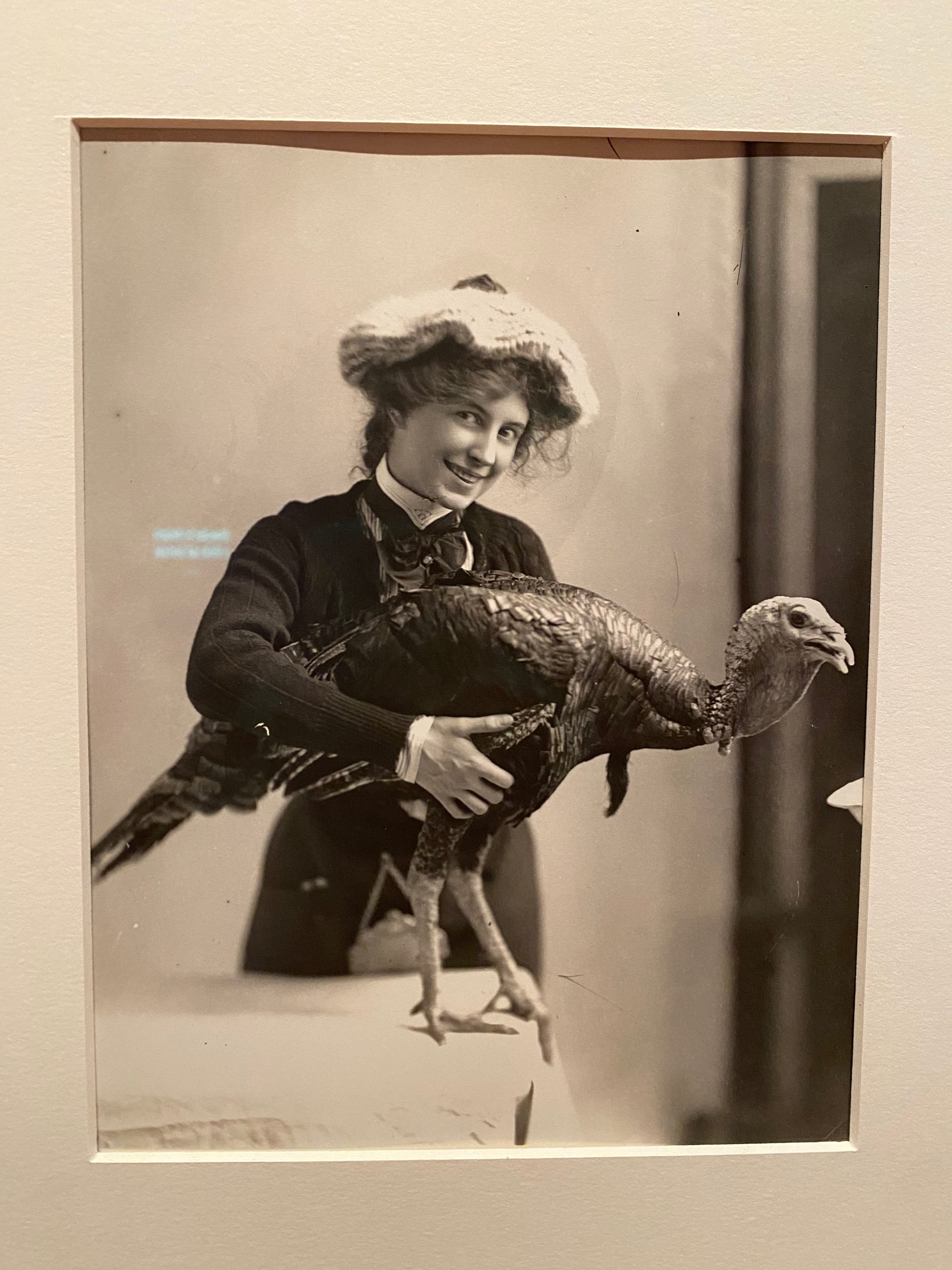 A photo of a historical photo of a woman in like 1900 or something, smiling and posing with a living turkey