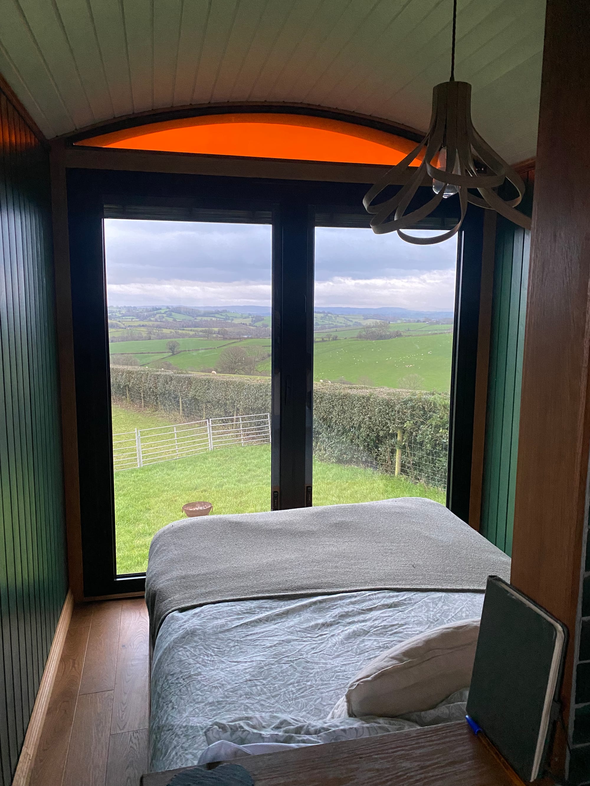 A photo of our luxury cottage in which you see our bed facing the windows that look out across a gorgeous view of sheep fields and rolling green hills