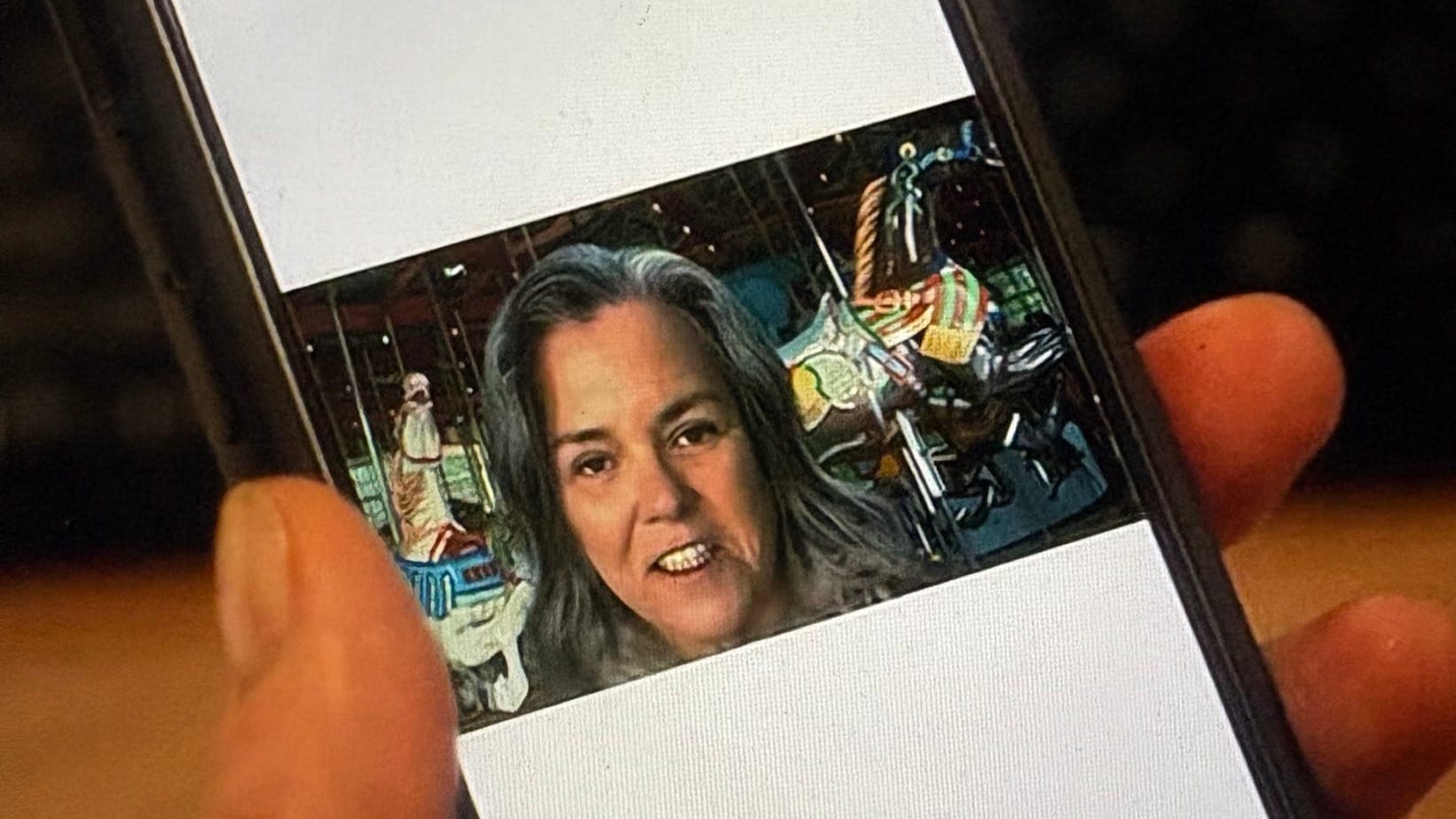 A still from And Just Like That showing Rosie O'Donnell's character in an extremely awkward selfie she took in front of the central park carousel
