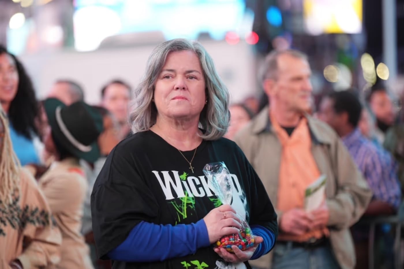 A still of Rosie O'Donnell in the new season of And Just Like that, wearing a Wicked musical t-shirt in the middle of Times Square