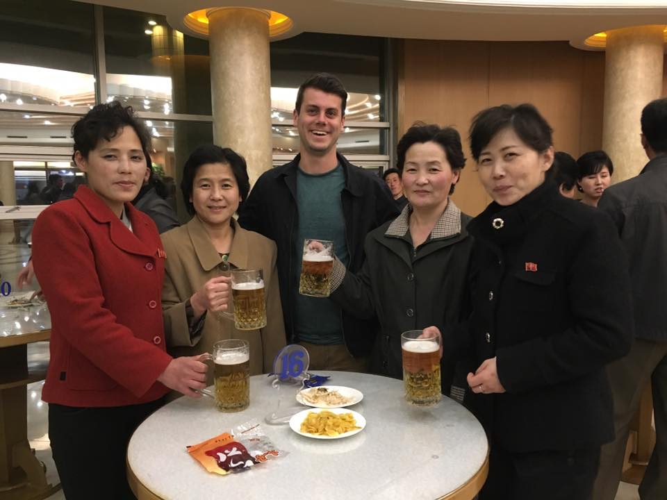 A photo of me, Danny, standing and smiling like an idiot at the camera, surrounded by 4 North Korean women, all holding mugs of beer and smiling at the camera. There are some snacks on the table I don't remember, and the scene seems normal but also what is "normal" in North Korea???